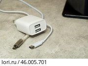 Блок питания с двумя портами USB и два кабеля USB-micro и USB Type-C и смартфон, на сером фоне. Адаптер питания, зарядное устройство для бытовой электроники. Редакционное фото, фотограф Sergei Gorin / Фотобанк Лори