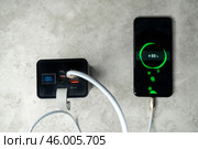 Смартфон запитан кабелем USB к пауэрбанку и заряжается на оранжевом фоне. Автономное зарядное устройство для бытовой электроники. Редакционное фото, фотограф Sergei Gorin / Фотобанк Лори