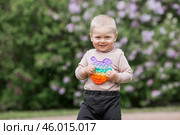 A beautiful chubby 2-year-old child in the park with a colorful Pop-it game. An anti-stress remedy. A pop It toy in children's hands. Стоковое фото, фотограф Photojuli / Фотобанк Лори