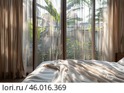 Sunlight streaming through sheer curtains onto unmade bed. Стоковое AI-изображение, AI-художник Иван Рябоконь / Фотобанк Лори