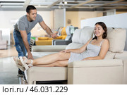 Smiling girl trying out sofa in furniture store, listening to salesman. Стоковое фото, фотограф Яков Филимонов / Фотобанк Лори