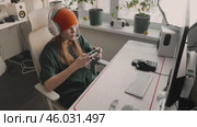 Woman balancing gaming and studies in stylish setup. Modern workspace with computer, monitor, headphones, microphone, and pc accessories emphasizes comfort, technology, and professional multitasking. Стоковое видео, видеограф Енваев Андрей / Фотобанк Лори