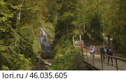 Active recreation in the mountains: tourists stroll through the dense forest alongside a mountain river, with picturesque waterfalls. Активный отдых в горах: туристы прогуливаются по густому лесу вдоль горной реки с живописными водопадами. Редакционное видео, видеограф Валерий Тесаков / Фотобанк Лори