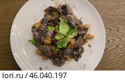 Warm salad with chicken liver in cream sauce with fried potatoes, mushrooms and mixed green salad in a white porcelain plate on a brown wooden table in an elite restaurant. Стоковое видео, видеограф worker / Фотобанк Лори