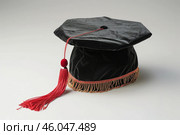 Black graduation doctoral cap with red tassel symbolizing academic achievement. Стоковое AI-изображение, AI-художник Иван Рябоконь / Фотобанк Лори