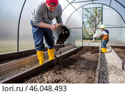 A male farmer pours new soil, soil for a new greenhouse. The concept of spring vegetable planting, greenhouse installation and farming. Стоковое фото, фотограф Photojuli / Фотобанк Лори
