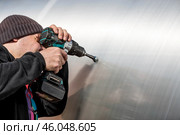 A man holds a battery-powered screwdriver and assembles a new greenhouse made of polyethylene, polycarbonate. Macro photography. Side view. Preparing for the spring garden season. Стоковое фото, фотограф Photojuli / Фотобанк Лори