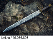 Sharp medieval sword lying on rocks outdoors. Стоковое AI-изображение, AI-художник Иван Рябоконь / Фотобанк Лори