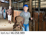Woman horse breeder carrying leather saddle. Стоковое фото, фотограф Яков Филимонов / Фотобанк Лори