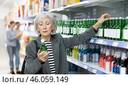 Elderly woman examining labels on bottles of soju in Asian store. Стоковое фото, фотограф Яков Филимонов / Фотобанк Лори
