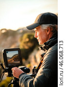 Videographer recording scenic landscape during golden hour. Стоковое AI-изображение, AI-художник Юрий Поздников / Фотобанк Лори