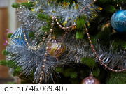 Новогодняя рождественская игрушка висит на ветке новогодней елки,  окутанная блестящей мишурой New Year's Christmas toy hangs on a New Year's tree branch, covered in shiny tinsel. Стоковое фото, фотограф Юрий Карачев / Фотобанк Лори