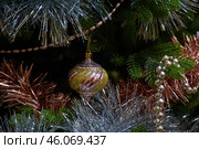 Новогодняя рождественская игрушка висит на ветке новогодней елки,  окутанная блестящей мишурой New Year's Christmas toy hangs on a New Year's tree branch, covered in shiny tinsel. Стоковое фото, фотограф Юрий Карачев / Фотобанк Лори