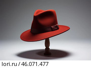 Elegant red hat resting on wooden stand in studio setting. Стоковое AI-изображение, AI-художник Иван Рябоконь / Фотобанк Лори