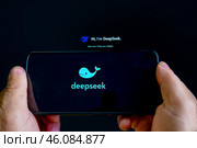 На экране телефона отображается логотип "deepseek". На заднем плане вы можете видеть экран компьютера с текстом: "Привет, я DeepSeek. Редакционное фото, фотограф Valeryi Vysotkov / Фотобанк Лори