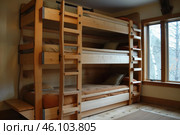 Triple bunk bed stands in rustic log cabin bedroom. Стоковое AI-изображение, AI-художник Иван Рябоконь / Фотобанк Лори