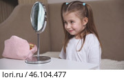 Fashion little girl in a white T-shirt is sitting at the dressing table in front of the mirror, smiling and winking her eyes. Advertising of children's cosmetics concept. Footage for kids blog. Стоковое видео, видеограф Ирина Михайличенко / Фотобанк Лори