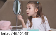 Fashion little girl in a white T-shirt is sitting at the dressing table in front of the mirror and applying makeup with eye shadow. Advertising of children's cosmetics concept. Footage for kids blog. Стоковое видео, видеограф Ирина Михайличенко / Фотобанк Лори