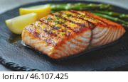 Grilled Salmon Fillet with a crispy skin, served with asparagus and lemon wedges on a black slate plate. Footage for culinary video blog. Стоковое AI-видео, аниматор Ирина Михайличенко / Фотобанк Лори