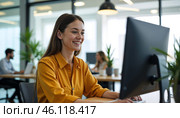 Женщина с улыбкой в жёлтой рубашке работает за компьютером в светлом современном офисном помещении. Стоковое AI-изображение, AI-художник Anna Leeva / Фотобанк Лори