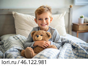 A cute boy hugs a teddy bear, sitting in a cozy bed, a small child hugs a toy and gets ready for bed. A healthy night's sleep. Стоковое AI-изображение, AI-художник Photojuli / Фотобанк Лори