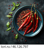 Atmospheric gastronomic photography featuring bright red hot chili peppers laid out on a dark blue plate. Ground and dried pepper pieces, as well as fresh green leaves, are scattered around the plate, creating an effective contrast against the dark background. The photo conveys a sense of piquancy, rich taste and oriental cuisine. The texture of the pepper is shiny, which emphasizes its freshness and spicy nature. The composition is made in the style of food photography with a play of light and shadow. Стоковое AI-изображение, AI-художник Анна Кривицкая / Фотобанк Лори