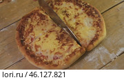 Round pizza is divided with a knife into several equal parts on a wooden table. homemade Italian cuisine. Стоковое видео, видеограф Strunov David / Фотобанк Лори
