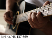 Playing the guitar. Strumming acoustic guitar. Musician plays music. Man fingers holding mediator. Man hand playing guitar neck in dark room. Unrecognizable person rehearsing, fretboard close-up. Стоковое фото, фотограф Марина Демидюк / Фотобанк Лори
