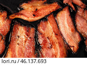 Frying Bacon Slices in a Pan. Crispy Pieces of Delicious Red Thin Smokey Bacon Fried in a Hot Skillet. Traditional Breakfast. Smoked Bacon Rasher or Strip Being Cooked. Grill. Fat High Calorie Food. Стоковое фото, фотограф Марина Демидюк / Фотобанк Лори