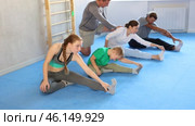 Family in gym during group sports training under guidance of trainer performs stretching on floor. Стоковое видео, видеограф Яков Филимонов / Фотобанк Лори