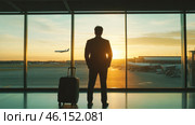 Businessman traveler in airport lounge looking out window at plane taking off at dawn. Business trip. Стоковое AI-изображение, AI-художник Елена Никишина / Фотобанк Лори