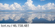 Calm ocean with fluffy clouds reflecting on water surface under blue sky, peaceful seascape with white clouds mirrored in still sea. Стоковое AI-изображение, AI-художник Павел Муравьев / Фотобанк Лори