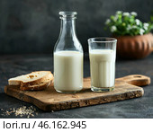 Органическое натуральное коровье молоко в стеклянной бутылке и стакане на стильной деревянной доске на каменном столе. Натуральные экологически чистые продукты. Стоковое AI-изображение, AI-художник Руслан Лесков / Фотобанк Лори