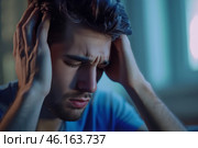 In a quiet room lit by soft blue light, a young man holds his head in frustration, reflecting his struggle with overwhelming stress and emotional turmoil late at night. Стоковое AI-изображение, AI-художник Sergey Grishin / Фотобанк Лори
