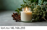 A mock-up of a comfortably burning candle made of glass with an empty white label and greenery in a home interior. Стоковое AI-изображение, AI-художник Photojuli / Фотобанк Лори