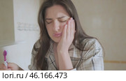 Girl brushes her teeth but feels pain, holding her cheek. Despite toothache, she continues caring for her oral health. Стоковое видео, видеограф Svetlana Golovco / Фотобанк Лори