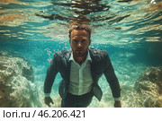 A man in an elegant business suit, who is underwater. The light penetrates the water surface, creating spectacular highlights on his face and clothes. His expression is serious, confident, as if he is moving towards a goal. Around him is transparent water with shades of turquoise, an underwater world with stones and reflections. This contrast between the strictness of the business image and the freedom of the underwater space creates a strong artistic effect. Стоковое AI-изображение, AI-художник Анна Кривицкая / Фотобанк Лори
