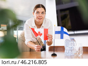 Positive young woman putting flag of Canada on the table with flag of Finland in conference room. Стоковое фото, фотограф Яков Филимонов / Фотобанк Лори