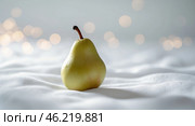 Fresh pear placed on textured white fabric with blurred background bokeh lights for a soft, aesthetic look. Стоковое AI-изображение, AI-художник Сергей Толмачёв / Фотобанк Лори