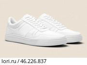 White leather lace-up running shoes with low tops, thick soles on a beige. The laces and rubber outsole. Sporty look. Men to wear during outdoor activities. Street hiking shoes. Trendy Male Boots Pair. Стоковое AI-изображение, AI-художник Марина Демидюк / Фотобанк Лори