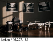 Ретро-камера и современный дрон на столе с развешенными на прищепках отпечатками фотографий в солнечном свете. Стоковое AI-изображение, AI-художник Сергей Никифоров-Гордеев / Фотобанк Лори