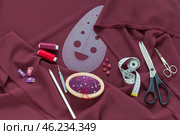 Top view of sewing accessories and materials for sew and cutting on burgundy silk fabric - threads, needles, buttons, scissors, pattern, pincushion. Sewing as a hobby. Flat lay, closeup, copy space. Стоковое фото, фотограф Виктория Катьянова / Фотобанк Лори