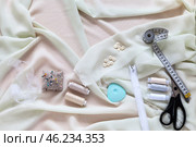 Top view of sewing accessories and materials for sew and cutting on white silk fabric - threads, needles, buttons, scissors, tailor chalk, pincushion, zip fastener. Sewing as a hobby. Flat lay, close-up. Стоковое фото, фотограф Виктория Катьянова / Фотобанк Лори