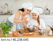 Mom and girl prepare dough for baking, mom adds salt to bowl, girl mixes ingredients with whisk. Стоковое фото, фотограф Яков Филимонов / Фотобанк Лори