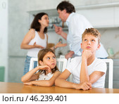 Two children sitting at the kitchen table sadly while their parents quarrelling. Стоковое фото, фотограф Яков Филимонов / Фотобанк Лори