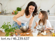 Mom and girl are talking in kitchen and mixing ingredients for pastry in bowl with whisk. Стоковое фото, фотограф Яков Филимонов / Фотобанк Лори
