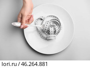 Female hand with plate, fork and measuring tape on grey background. Concept of anorexia. Стоковое фото, фотограф Pixel_shot / Фотобанк Лори