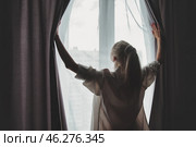 Morning Light Streams Through the Window as a Woman Draws Back the Curtains. Стоковое фото, фотограф Aleksandr Golubev / Фотобанк Лори