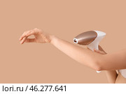 Beautiful young woman epilating her arms with modern photoepilator on brown background. Стоковое фото, фотограф Pixel_shot / Фотобанк Лори