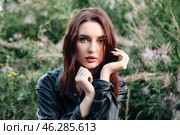 Bathed in soft golden light, a young woman poses gracefully among vibrant greenery and blooming flowers, embodying serenity and confidence with a gentle yet captivating expression. Стоковое фото, фотограф Aleksandr Golubev / Фотобанк Лори